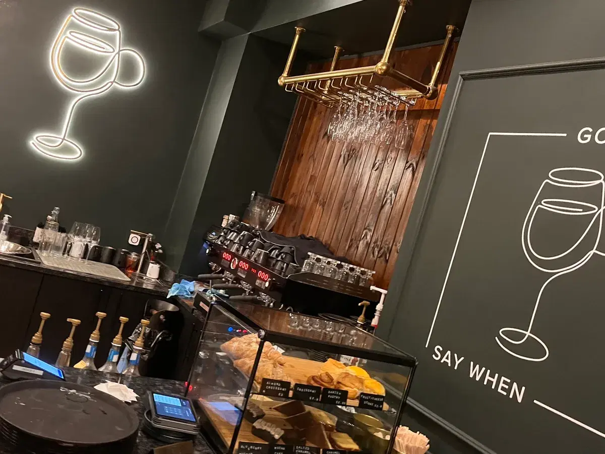 Inside Say When on Gosforth High Street — dark green walls, a brass wine rack and the neon wine-glass sign